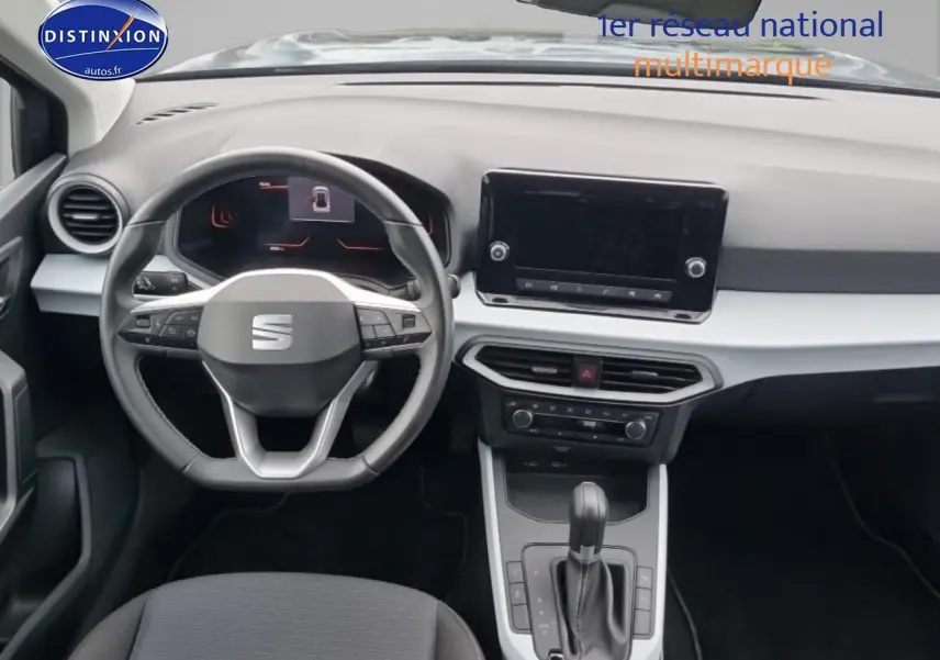 Vue intérieure frontale du tableau de bord gris clair et noir du SEAT Arona 2025 avec volant multifonction et écran tactile central.