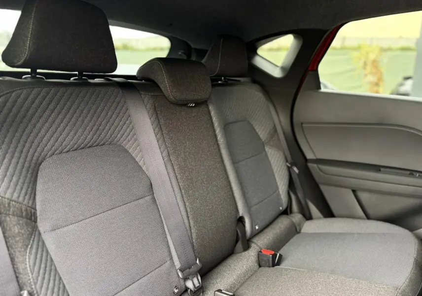 Vue intérieure arrière du Renault Captur 2025, sièges tissu gris avec ceinture de sécurité centrale visible et partie de la porte côté droit rouge Flamme.