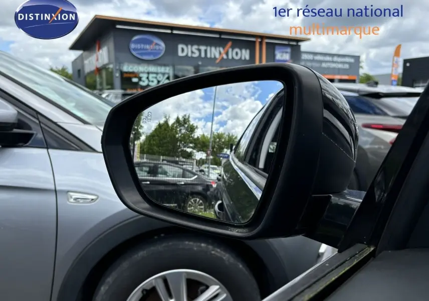 Rétroviseur côté gauche d’un Opel Grandland X noir, avec reflet sur un parking et bâtiment Distinxion en arrière-plan.