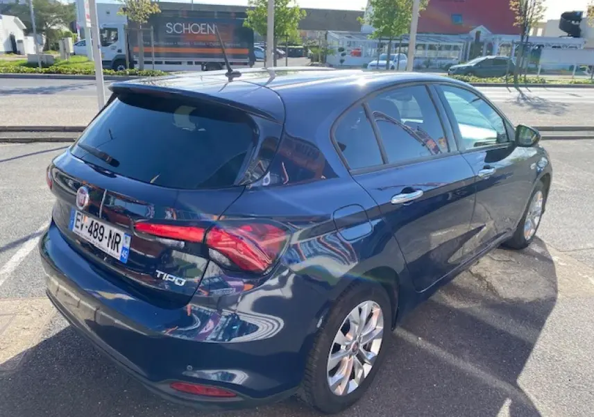 Vue 3/4 arrière droite d'une Fiat Tipo bleu métallisé avec vitres surteintées et feux arrière allumés.