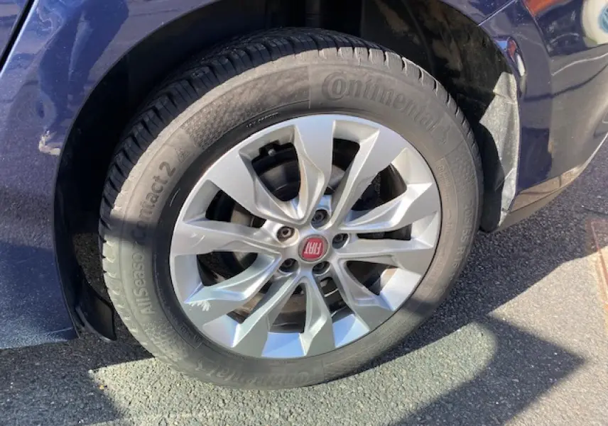 Gros plan sur la roue avant gauche d’une FIAT TIPO bleu métallisé avec jante argentée et logo rouge FIAT au centre.