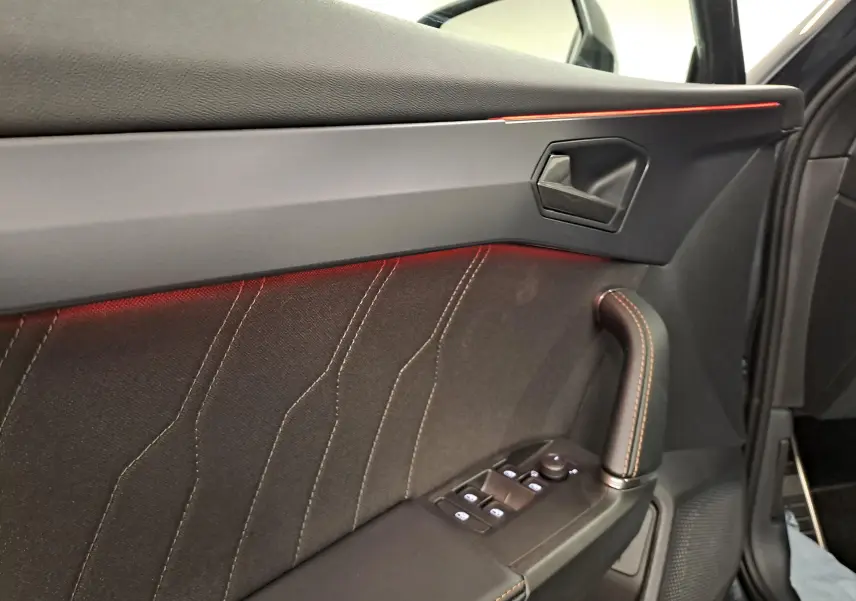 Détail de la porte côté gauche du CUPRA Formentor gris magnétique, avec éclairage d'ambiance rouge et surpiqûres cuivrées.