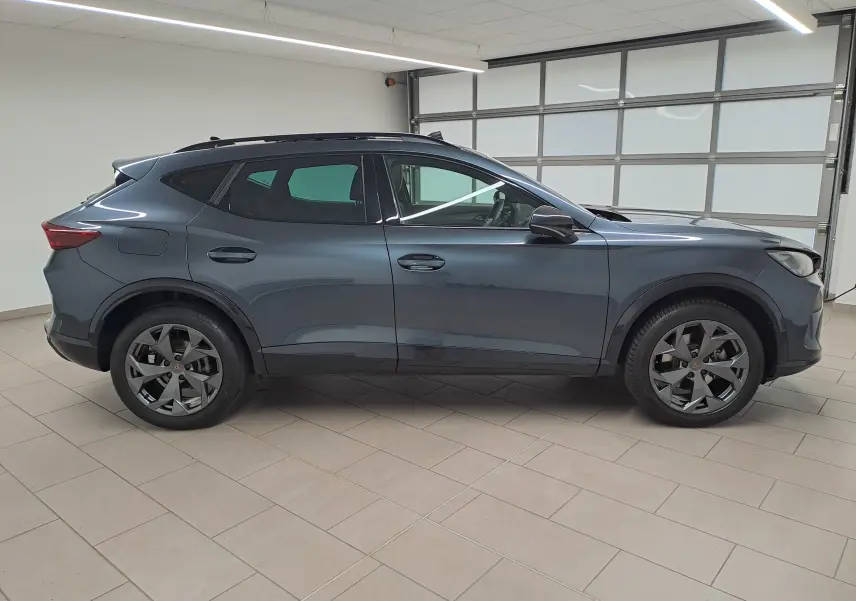 Vue de profil côté gauche d'un CUPRA Formentor gris magnétique avec jantes alliage et toit ouvrant panoramique en intérieur showroom.
