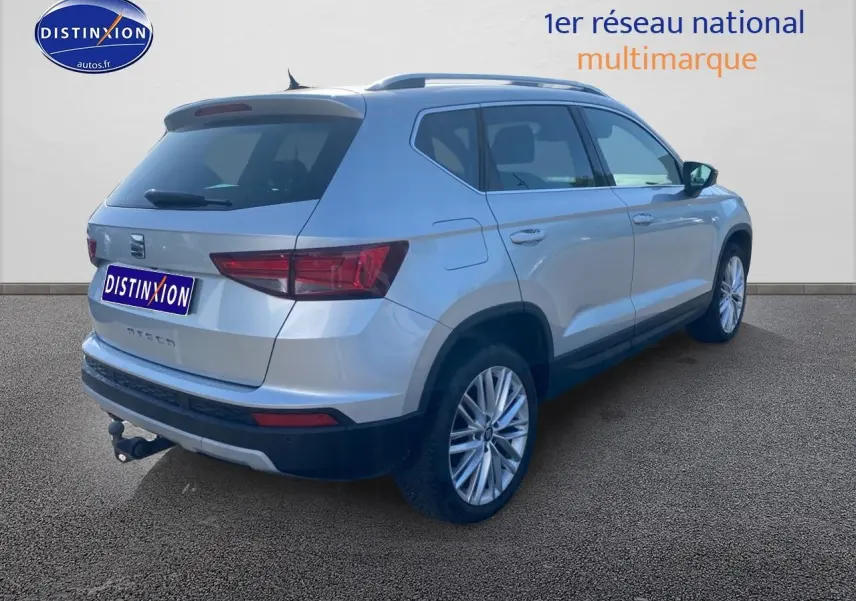 Vue 3/4 arrière droite d’un SEAT Ateca gris avec jantes alu et attelage visible sur fond neutre.