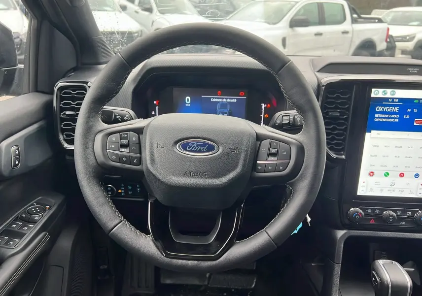 Vue intérieure centrée sur le volant cuir multifonctions du Ford Ranger gris carbone avec écran tactile vertical et commandes au volant.