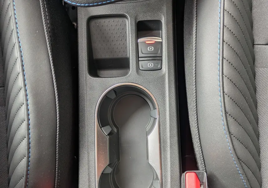 Vue plongeante sur la console centrale noire avec porte-gobelets et boutons de frein à main et auto-hold du Renault Symbioz gris Rafale.