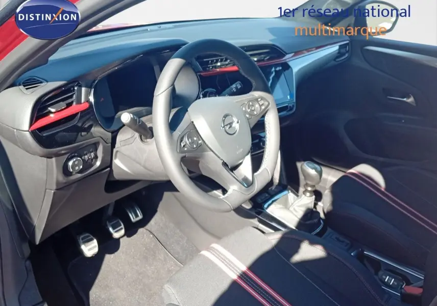 Vue intérieure côté conducteur de l’Opel Corsa rouge métal 2023 avec volant multifonction et levier de vitesse manuel.