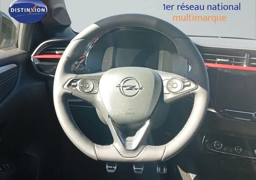 Vue rapprochée du volant noir de l’Opel Corsa 2023, avec tableau de bord et détails rouges en arrière-plan.