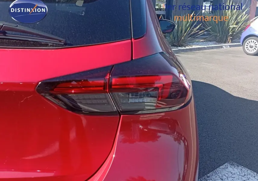 Vue arrière droite d'une Opel Corsa rouge métal avec toit noir, mettant en valeur le feu arrière moderne et la carrosserie brillante.