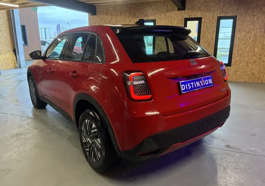 Vue 3/4 arrière droite d'une FIAT 600 1.2 Hybrid 100 rouge avec toit noir et feux arrière LED dans un garage.