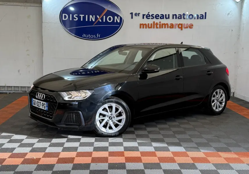 Audi A1 noire vue en 3/4 avant droit dans un showroom avec sol à damiers gris et orange.