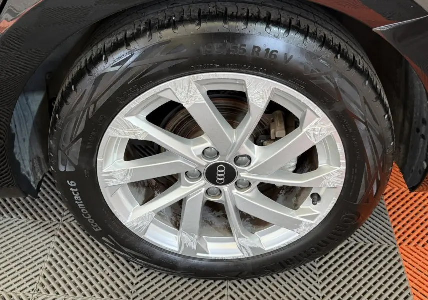 Gros plan sur la roue avant droite d'une Audi A1 noire, jante alliage argent avec logo Audi au centre.