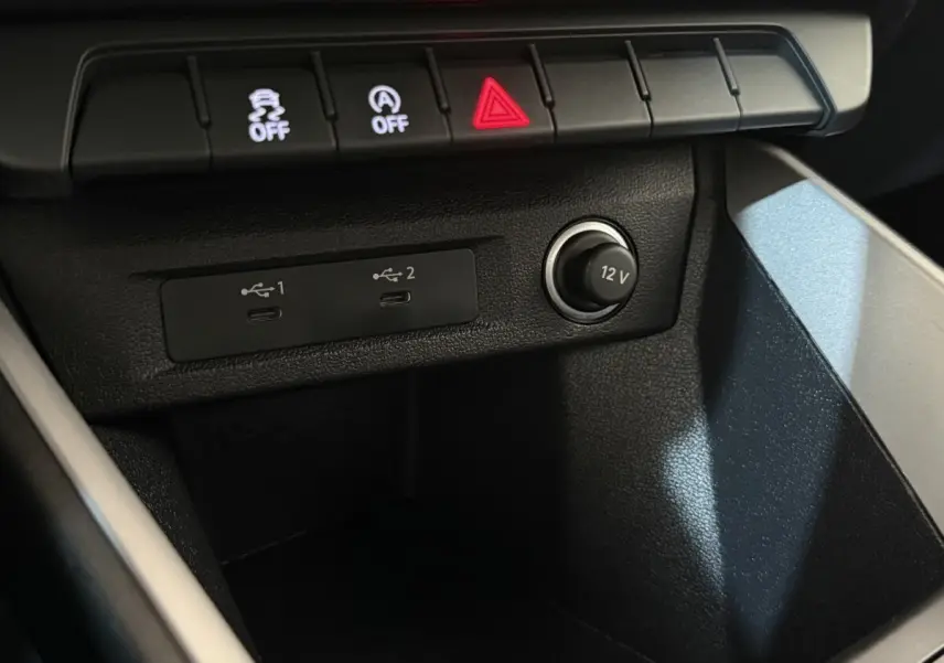 Vue rapprochée de la console centrale noire de l’Audi A1 2021, montrant prises USB et prise 12V avec boutons de contrôle.