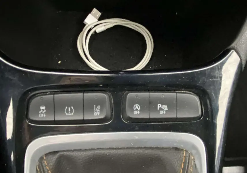 Gros plan sur la console centrale de l’Opel Crossland X 2020, montrant les boutons de contrôle et un câble USB blanc.