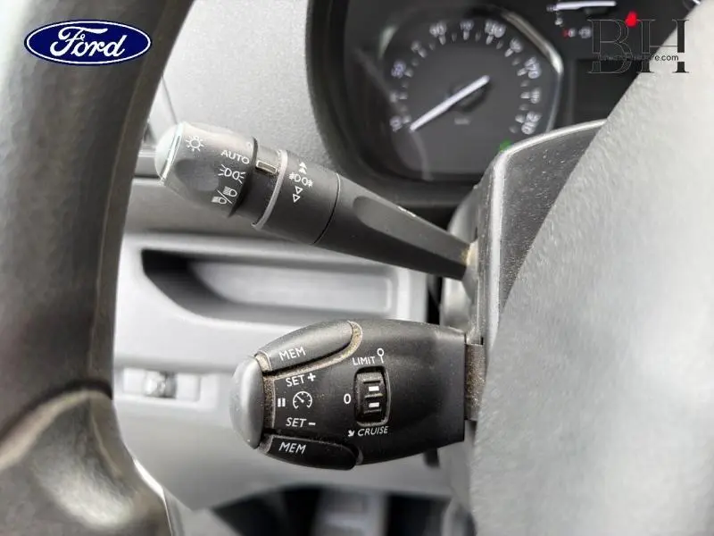 Gros plan sur les commandes de régulateur de vitesse et éclairage derrière le volant d'un Peugeot Expert Fourgon blanc.