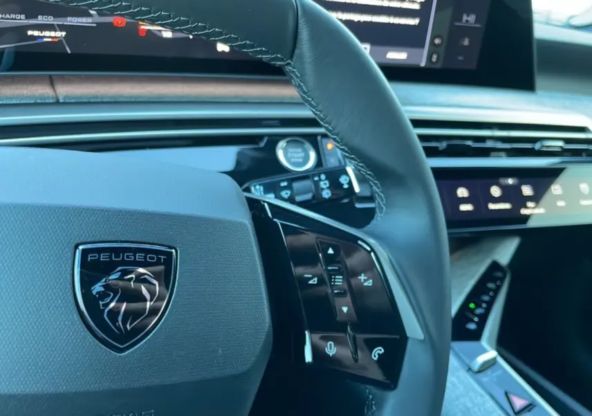 Gros plan sur le volant cuir multifonctions Peugeot 5008 Hybrid 2026 avec tableau de bord numérique et commandes tactiles.