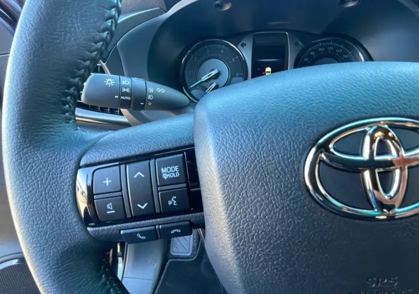 Gros plan sur le volant noir du Toyota Hilux 2025 avec commandes intégrées et tableau de bord visible en arrière-plan.