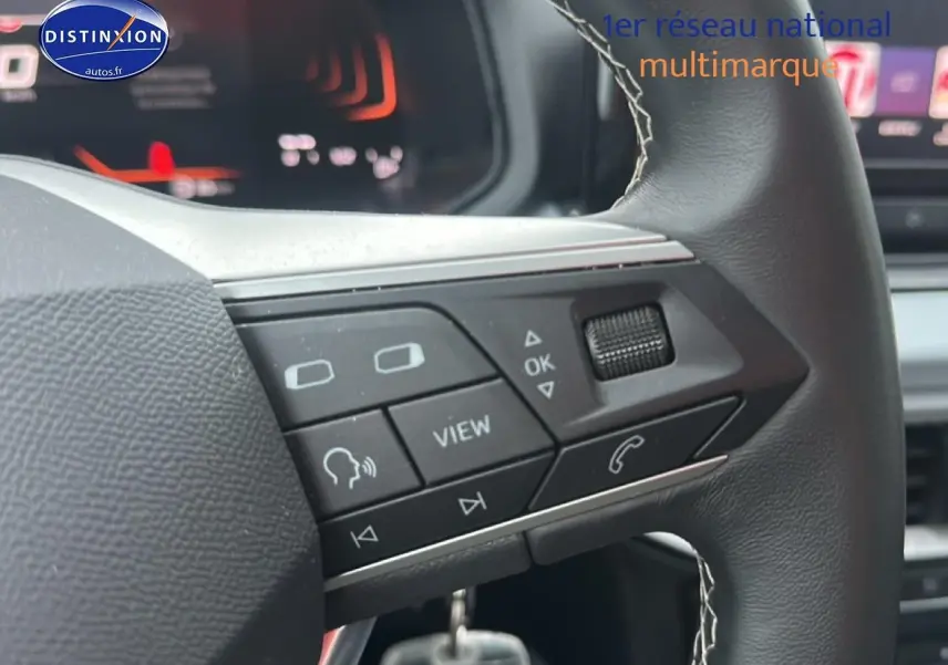 Gros plan sur les commandes multifonctions du volant cuir noir du SEAT Arona 2025, avec affichage digital en arrière-plan.