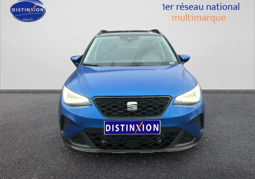Vue frontale d'un SEAT Arona bleu saphir avec phares allumés et calandre noire au logo central.