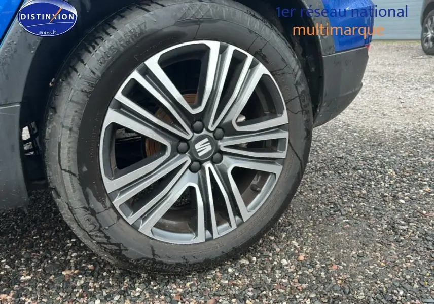 Gros plan sur la jante avant droite en alliage gris et noir du SEAT Arona bleu saphir, avec logo central Seat visible.