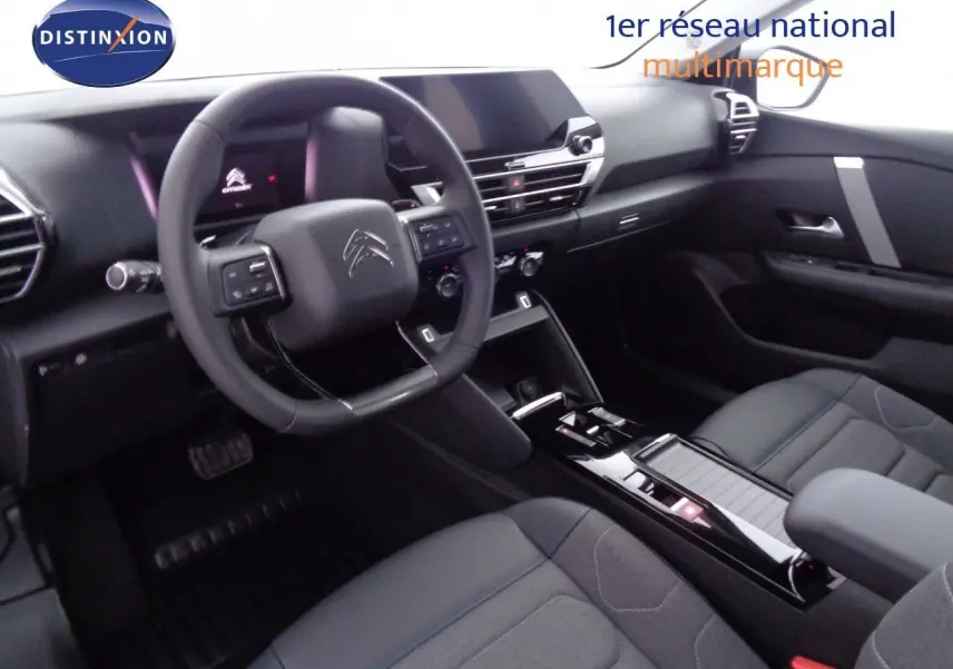 Intérieur de la Citroën C4 2023 en gris, vue côté conducteur montrant le tableau de bord et la console centrale moderne.