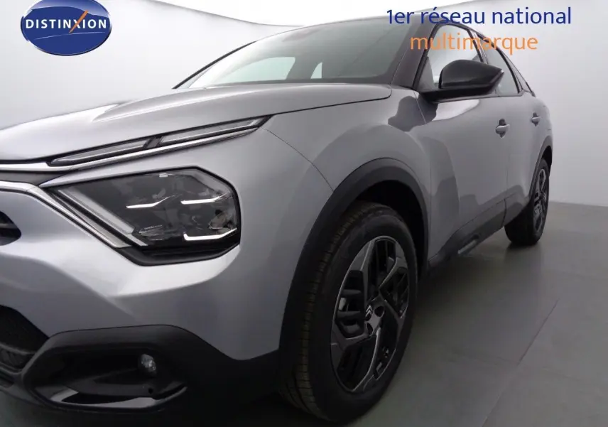 Vue 3/4 avant droit d'une Citroën C4 2023 gris Artense métal avec phares modernes et jantes noires distinctives.