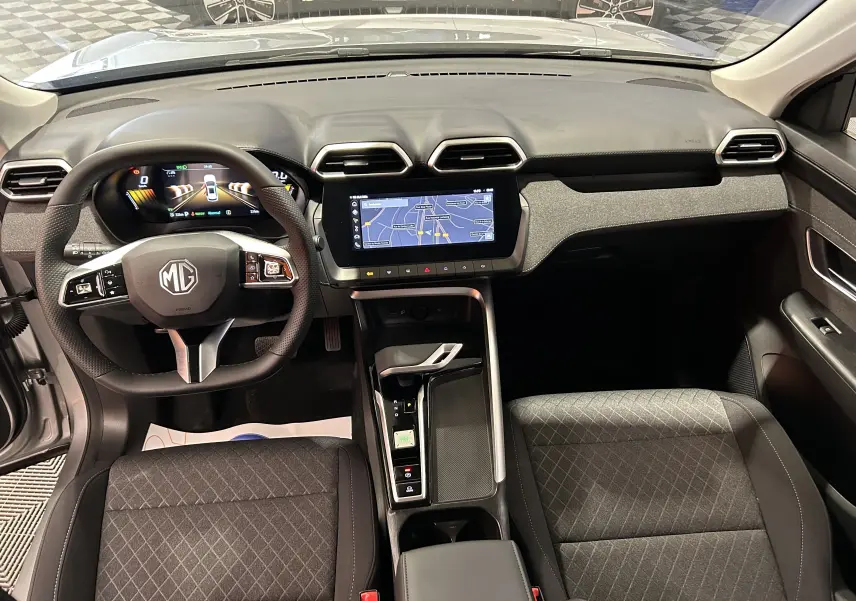 Vue intérieure avant du MG ZS Cosmic Silver 2025, avec tableau de bord numérique et écran tactile central affichant la navigation.