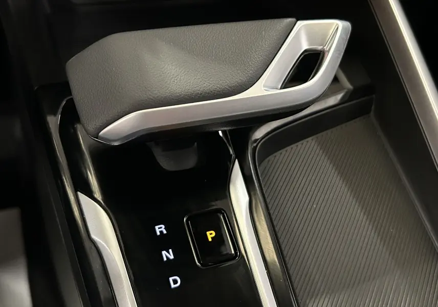 Gros plan sur la commande de boîte automatique noire et argentée du MG ZS hybride, avec le mode parking éclairé en jaune.