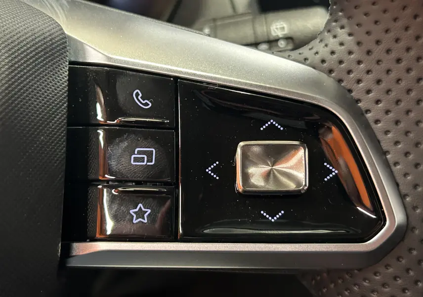 Gros plan sur les commandes noires et argentées au volant perforé du MG ZS Cosmic Silver 2025, version hybride.