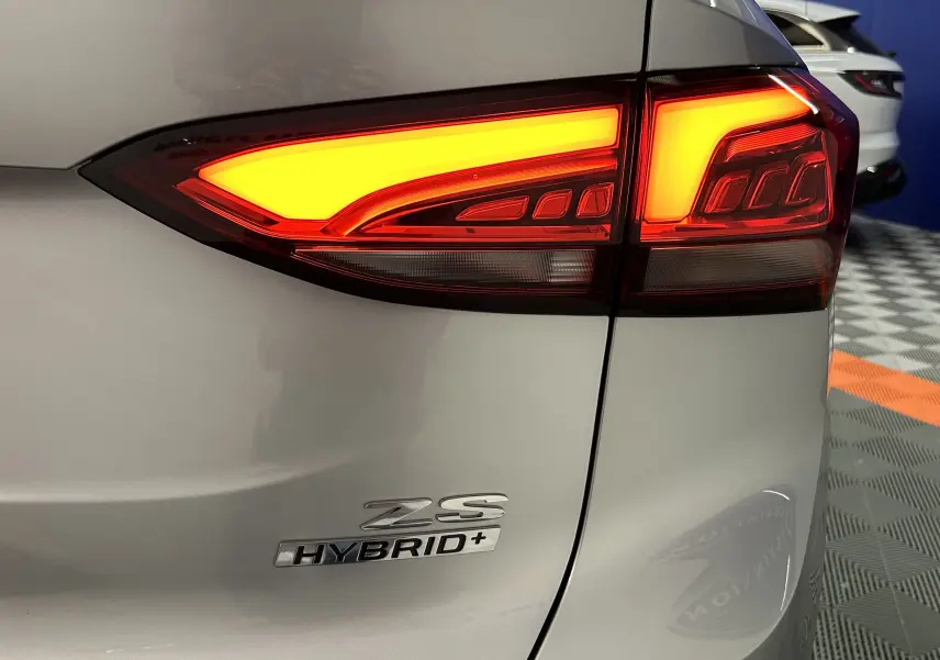 Gros plan sur le feu arrière droit allumé d’un MG ZS Cosmic Silver 2025 avec logo Hybrid+ visible.