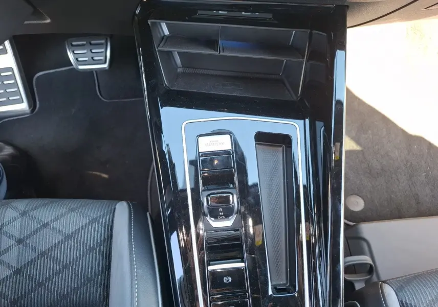 Vue plongeante sur la console centrale noire brillante de la Volkswagen Golf blanche, avec levier de vitesses DSG et bouton start/stop.