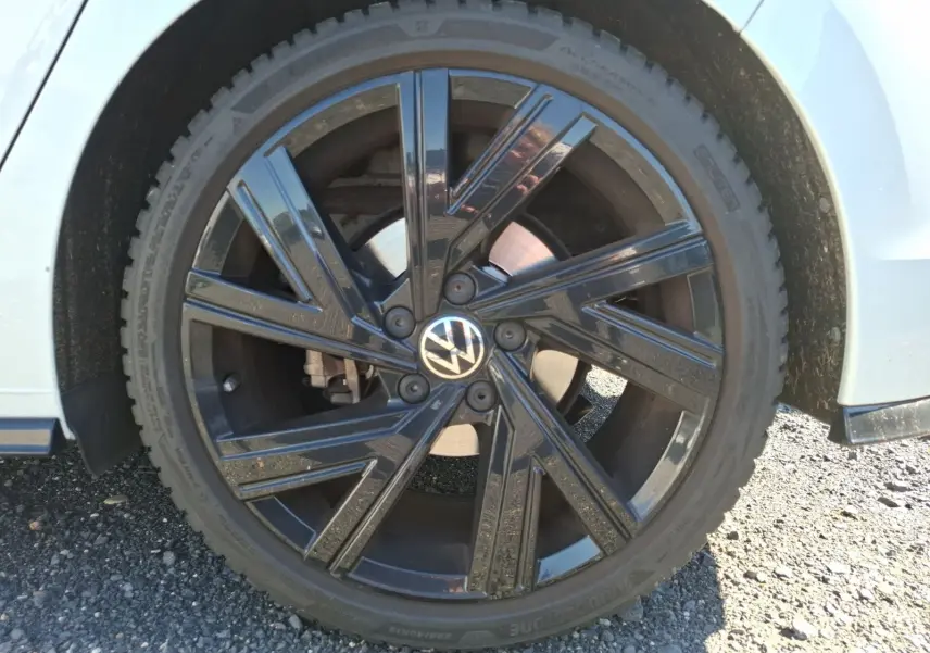 Gros plan sur la jante noire brillante côté gauche d'une Volkswagen Golf blanche 2023, avec logo VW au centre.