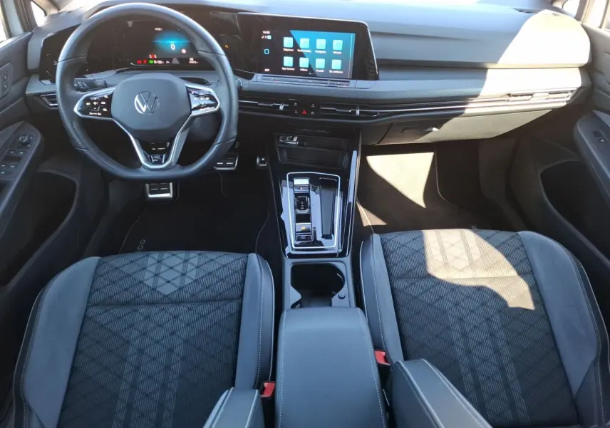 Vue intérieure avant de la Volkswagen Golf 1.5 E-TSI R-Line 2023, montrant le volant, l’écran tactile et les sièges sport noirs.