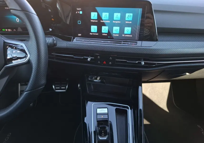 Vue intérieure centrée sur la console et l’écran tactile de la Volkswagen Golf blanche, avec volant et commandes visibles.