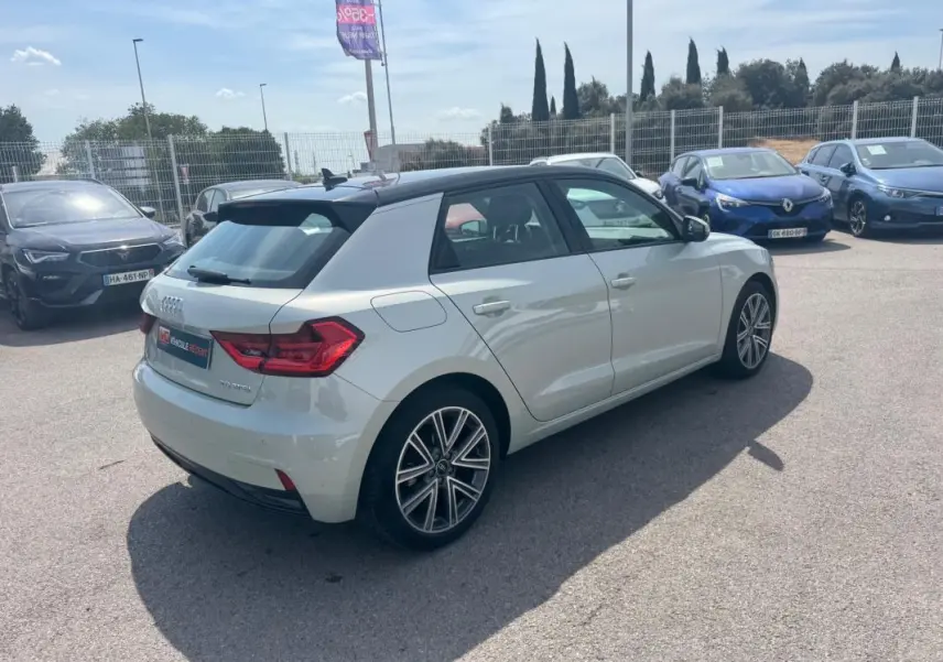 Audi A1 Sportback gris vue 3/4 arrière droit sur parking, avec toit noir et jantes alliage distinctives.