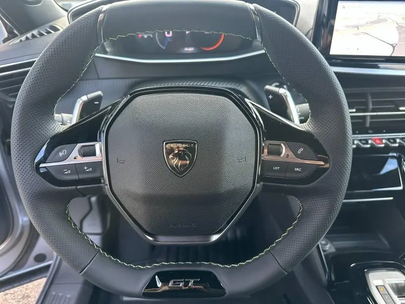 Volant cuir noir avec surpiqûres vertes et logo Peugeot GT au centre, vue rapprochée de l'habitacle du 2008 hybride.