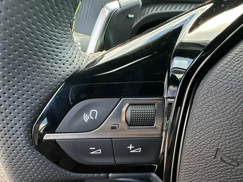 Gros plan sur les commandes noires du volant cuir perforé du Peugeot 2008 Hybrid bleu, avec molette et boutons volume.