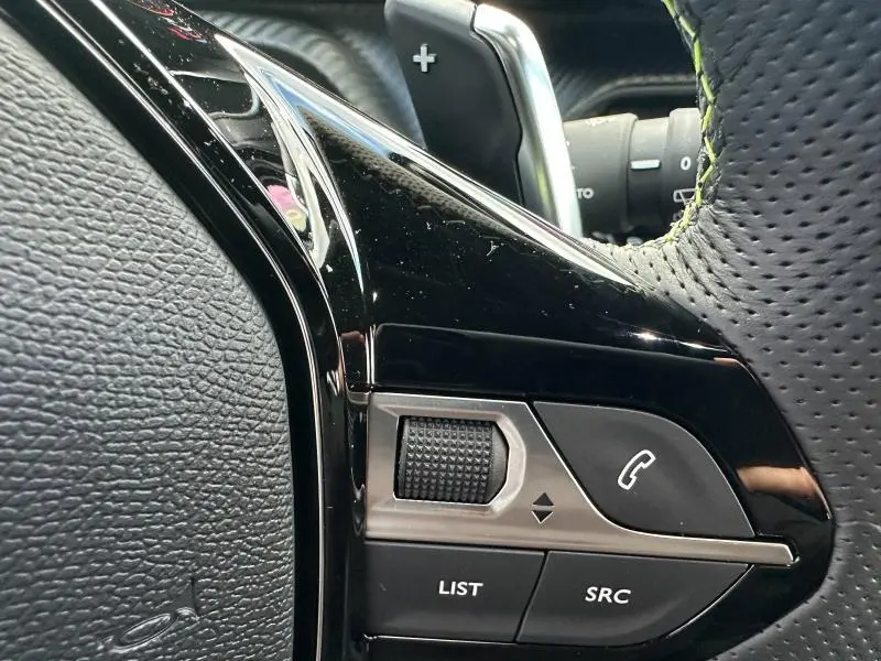 Gros plan sur les commandes du volant cuir perforé noir du Peugeot 2008 Hybrid bleu, avec molette et bouton téléphone.