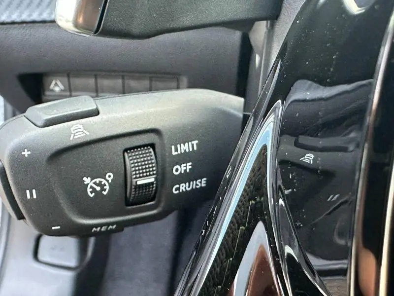 Gros plan sur la commande de régulateur de vitesse du Peugeot 2008 Hybrid bleu, avec molette et inscriptions blanches.