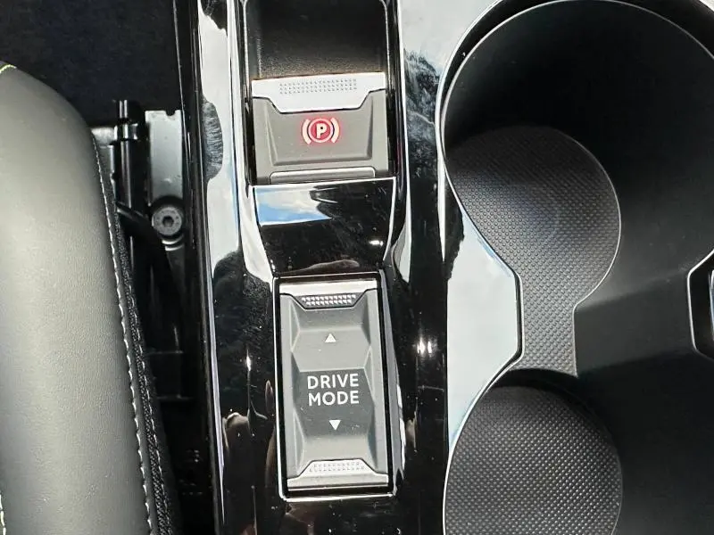 Gros plan sur la console centrale noire brillante du Peugeot 2008 Hybrid avec bouton Drive Mode et frein à main électronique.