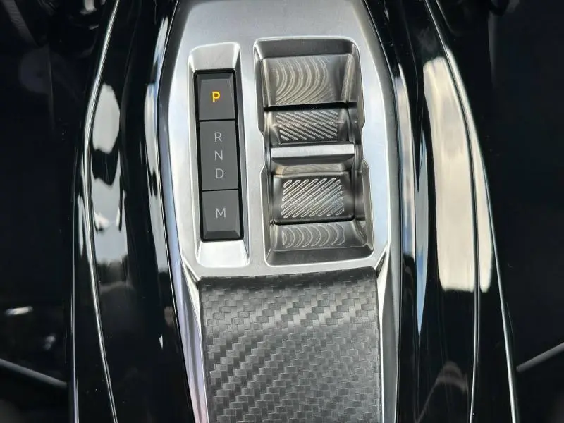 Gros plan sur la console centrale du Peugeot 2008 Hybrid avec sélecteur de boîte auto et finition carbone noire.
