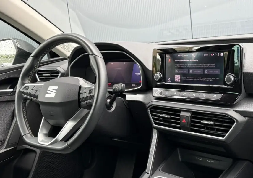 Vue intérieure côté conducteur du tableau de bord du SEAT Leon 2024 avec écran tactile et volant multifonction noir.