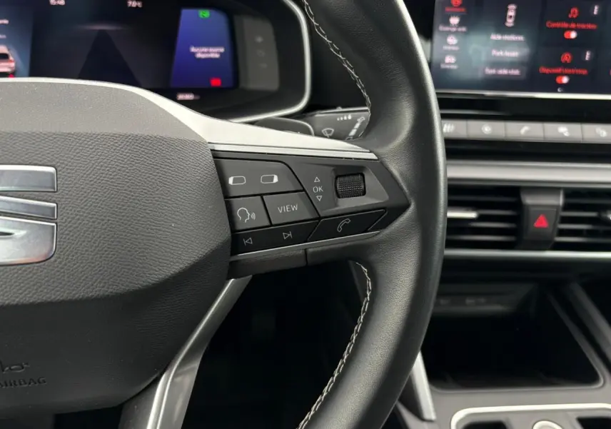 Gros plan sur le volant cuir noir de la SEAT LEON 2024 avec commandes multifonctions et combiné digital en arrière-plan.