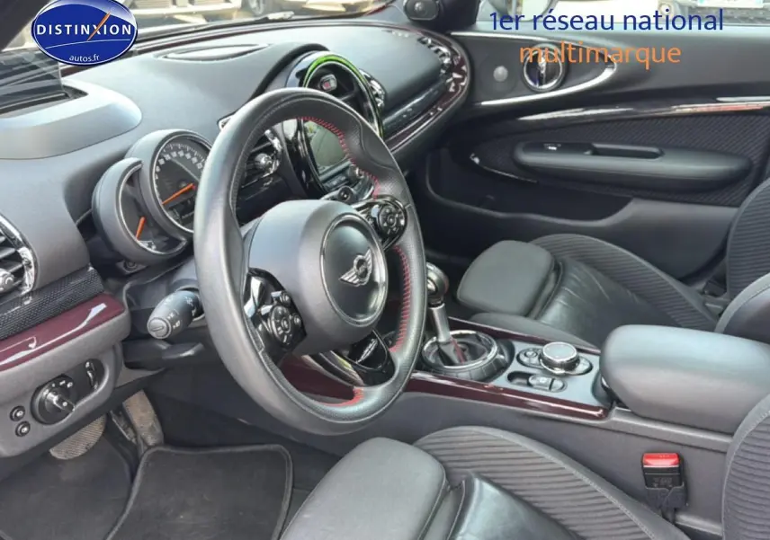 Vue intérieure côté conducteur de la MINI Clubman bordeaux, volant cuir sport et console centrale avec finitions chromées.
