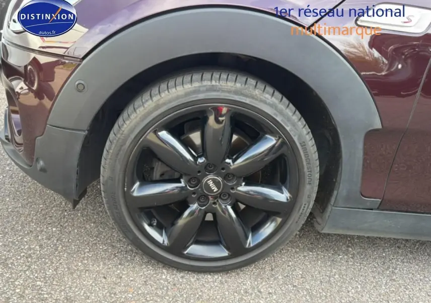 Gros plan sur la roue avant gauche noire brillante d'une MINI Clubman F54 bordeaux, avec logo MINI au centre.