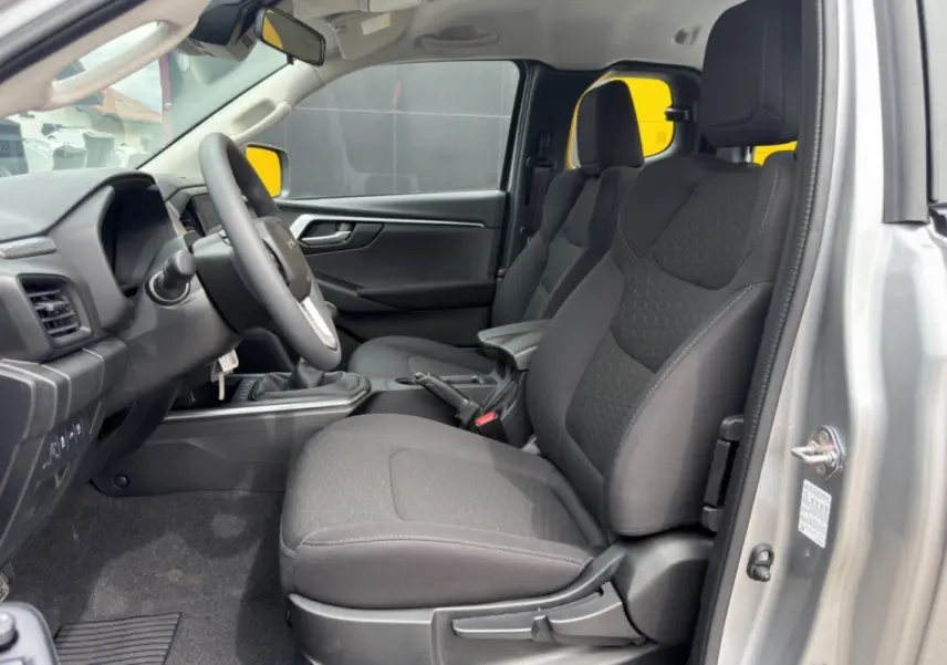 Vue intérieure côté conducteur de l'Isuzu D-MAX 2026 en Mercury silver metal, sièges tissu gris et accoudoir central.