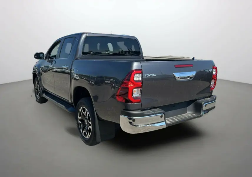 Toyota Hilux 4x4 gris atlas vu 3/4 arrière droit, avec jantes alu 18 pouces et marchepieds chromés.