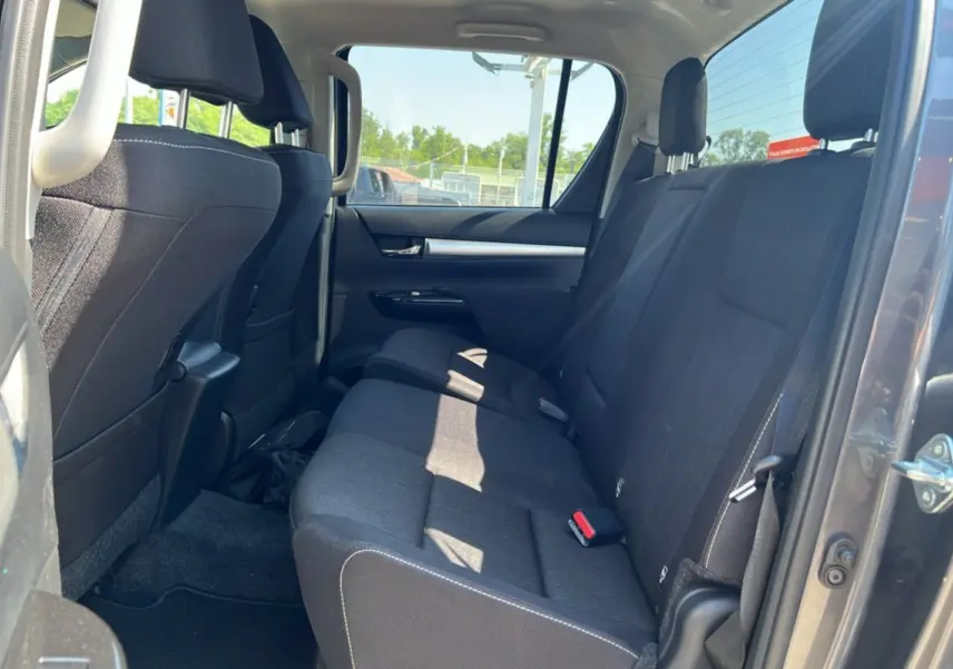Vue intérieure arrière montrant la banquette tissu noire du Toyota Hilux 4x4 gris atlas avec porte ouverte côté droit.