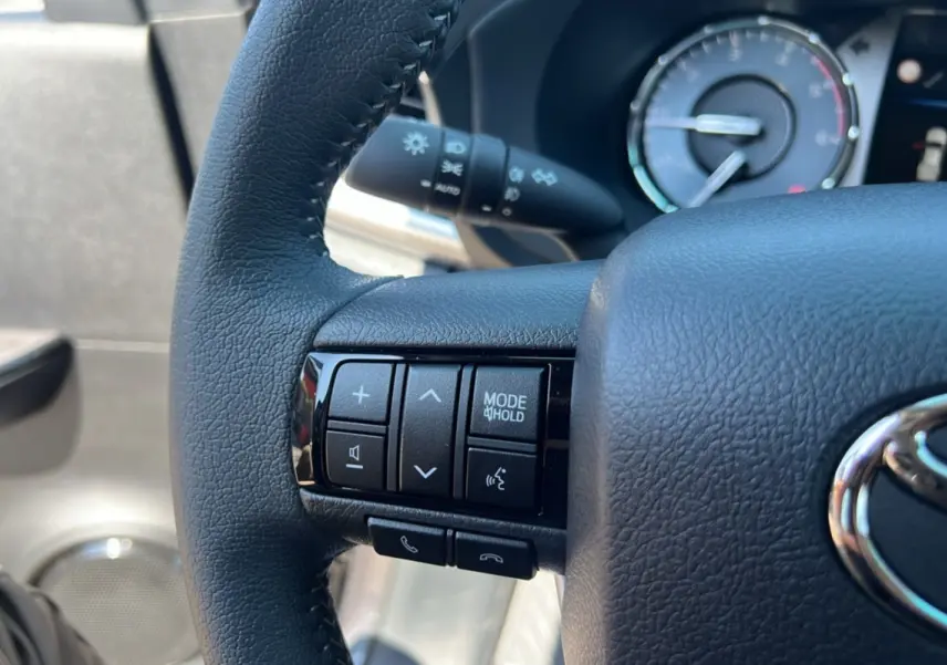Gros plan sur le volant cuir noir du Toyota Hilux 2026, avec commandes multifonctions visibles côté gauche.