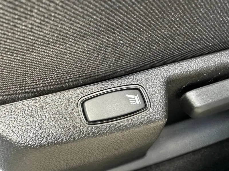 Bouton de réglage lombaire noir sur le côté gauche du siège en tissu brun cuivré du Dacia Duster blanc 2024.